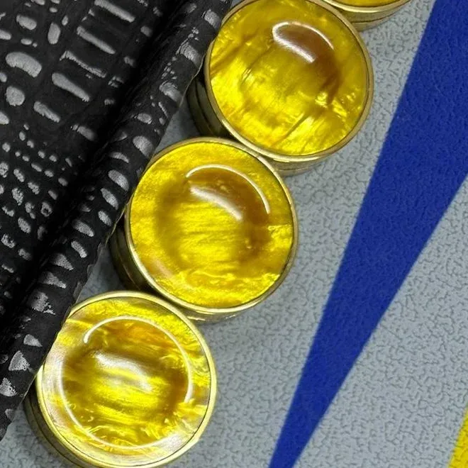 Yellow checkers with brass rims set out along the edge of a board